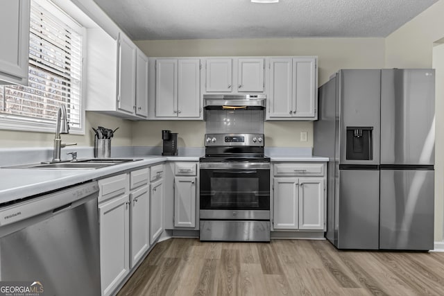 kitchen featuring sink, white cabinetry, a textured ceiling, light wood-type flooring, and appliances with stainless steel finishes