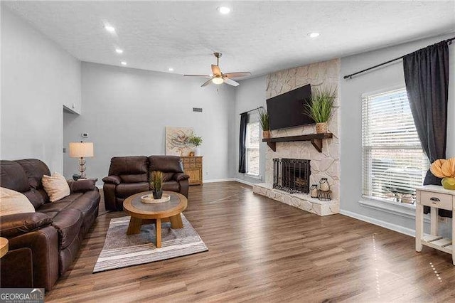 living room featuring ceiling fan, a stone fireplace, dark hardwood / wood-style floors, and a textured ceiling