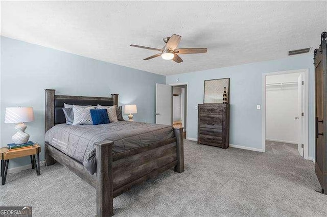 bedroom featuring a spacious closet, ceiling fan, a barn door, light carpet, and a textured ceiling