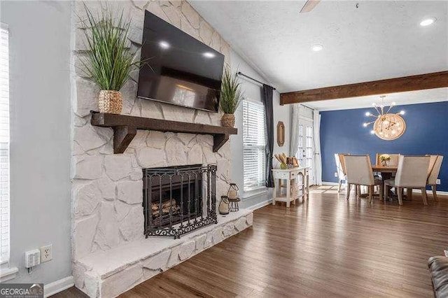 living room with hardwood / wood-style flooring, a stone fireplace, beam ceiling, and a textured ceiling