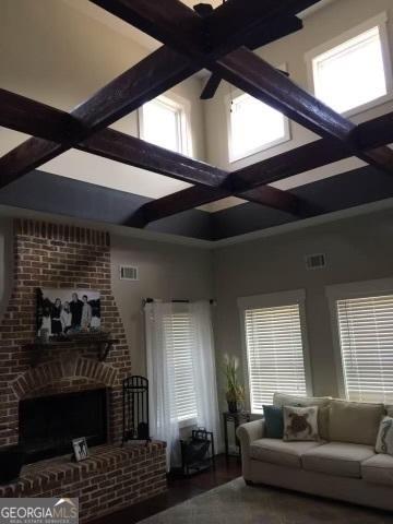 living room featuring a towering ceiling, coffered ceiling, wood-type flooring, a brick fireplace, and beamed ceiling