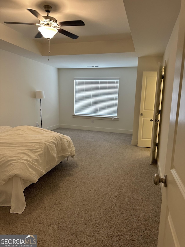 carpeted bedroom featuring a raised ceiling and ceiling fan