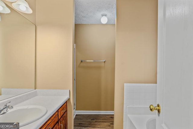 bathroom with wood-type flooring, a bath, vanity, and a textured ceiling