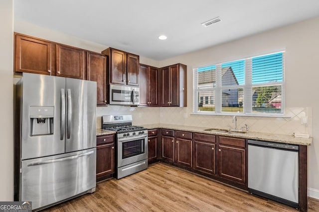 kitchen with sink, appliances with stainless steel finishes, tasteful backsplash, light stone countertops, and light wood-type flooring