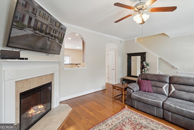 living room with a tiled fireplace, ornamental molding, ceiling fan, and light hardwood / wood-style flooring