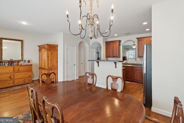 dining room with ceiling fan with notable chandelier, sink, and light wood-type flooring