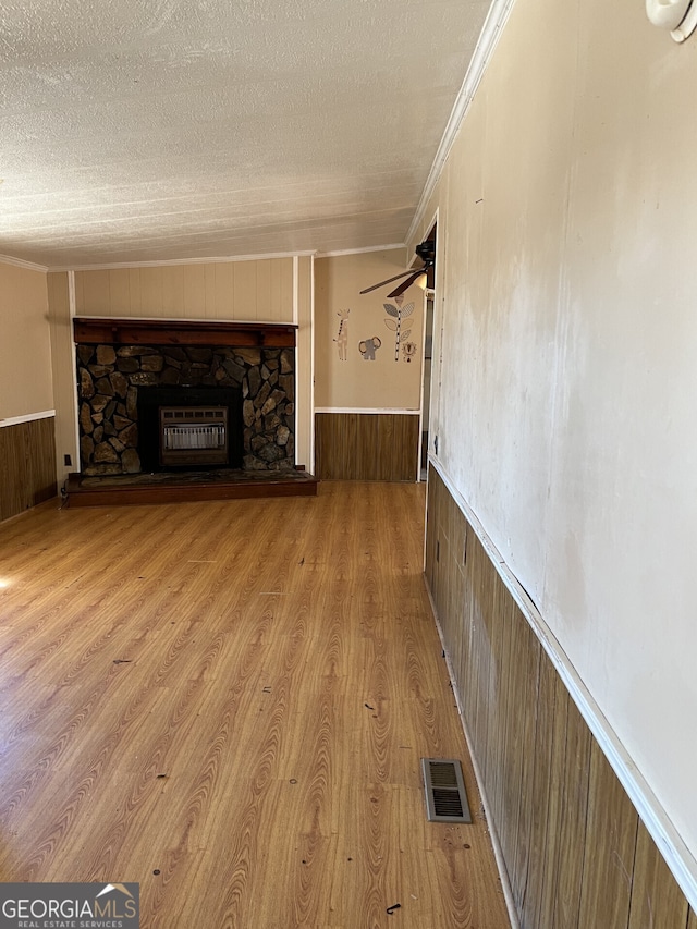 unfurnished living room featuring ornamental molding, a fireplace, a textured ceiling, and wood walls