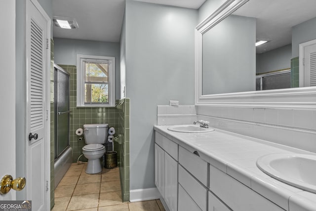 full bathroom featuring toilet, combined bath / shower with glass door, tile walls, vanity, and tile patterned flooring