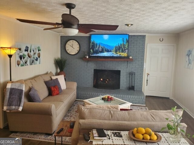 living room with wood-type flooring, a brick fireplace, ceiling fan, and a textured ceiling