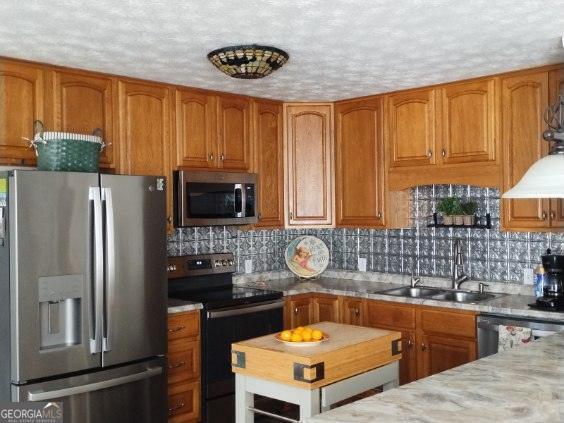 kitchen with appliances with stainless steel finishes, light stone countertops, sink, and decorative backsplash