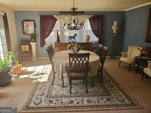 dining room featuring ornamental molding, carpet, a textured ceiling, and a chandelier