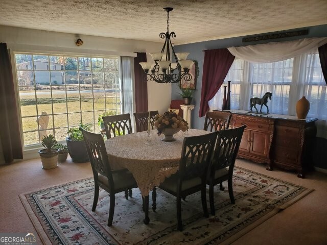 dining area featuring an inviting chandelier, carpet floors, a wealth of natural light, and a textured ceiling