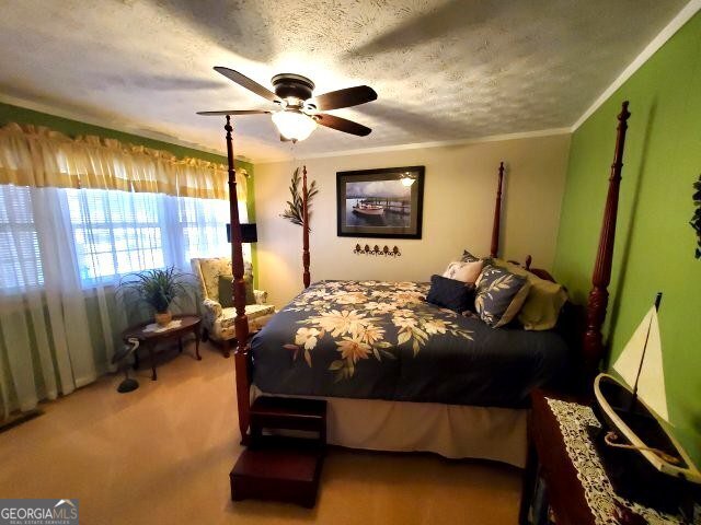 carpeted bedroom featuring ornamental molding, ceiling fan, and a textured ceiling