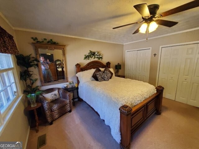 carpeted bedroom featuring ornamental molding, two closets, and ceiling fan