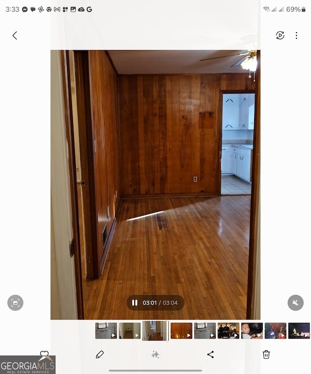 unfurnished room featuring hardwood / wood-style flooring, ceiling fan, and wood walls