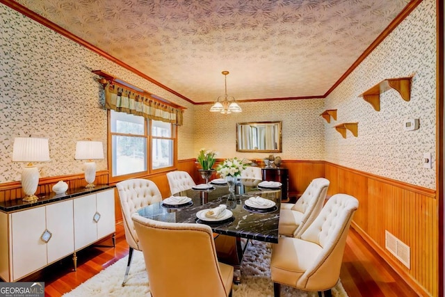 dining area featuring hardwood / wood-style flooring, ornamental molding, a chandelier, and a textured ceiling