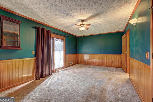 spare room featuring ceiling fan, light colored carpet, a textured ceiling, and wood walls