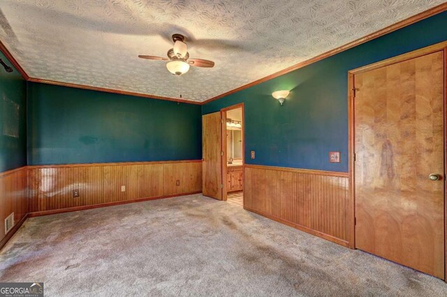 unfurnished room with wood walls, ornamental molding, ceiling fan, light carpet, and a textured ceiling