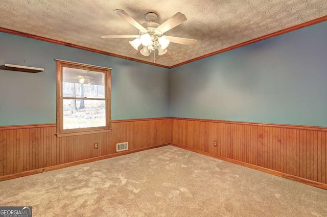 spare room with wooden walls, ceiling fan, crown molding, light carpet, and a textured ceiling