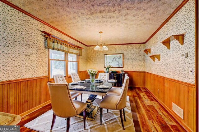 dining area with a notable chandelier, ornamental molding, wood-type flooring, and a textured ceiling