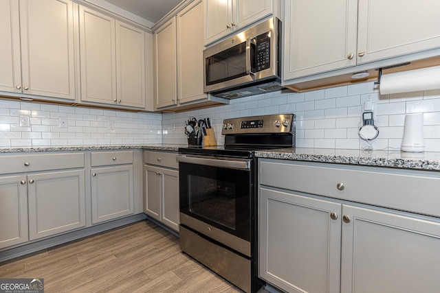 kitchen with appliances with stainless steel finishes, gray cabinetry, light stone countertops, decorative backsplash, and light wood-type flooring