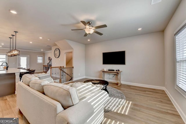 living room featuring crown molding, sink, ceiling fan with notable chandelier, and light wood-type flooring