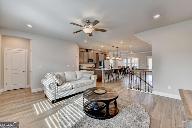 living room featuring sink, ceiling fan with notable chandelier, and light hardwood / wood-style floors