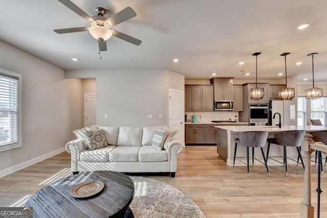 living room with sink, ceiling fan with notable chandelier, and light wood-type flooring