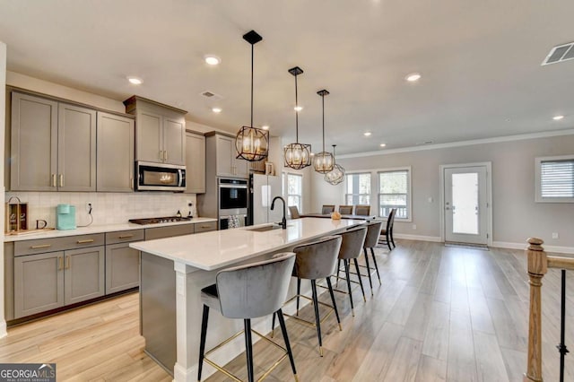 kitchen with gray cabinets, a breakfast bar, stainless steel appliances, an island with sink, and decorative backsplash