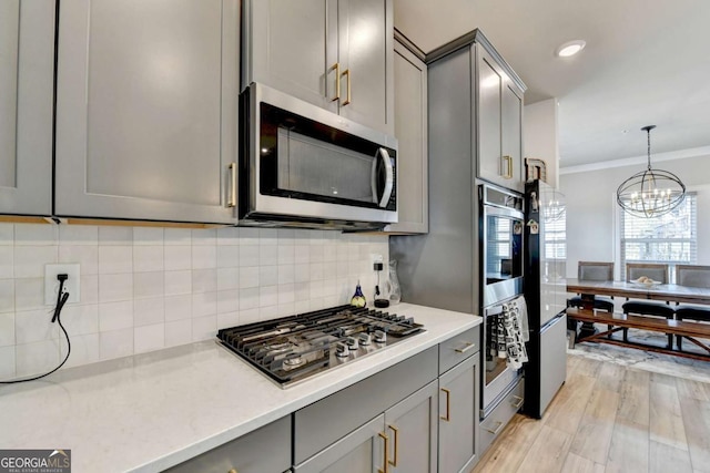 kitchen with crown molding, gray cabinets, stainless steel appliances, tasteful backsplash, and decorative light fixtures