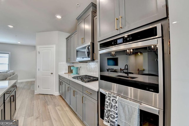 kitchen with tasteful backsplash, gray cabinets, stainless steel appliances, and light hardwood / wood-style flooring