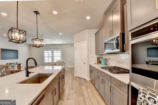 kitchen featuring appliances with stainless steel finishes, sink, backsplash, hanging light fixtures, and light wood-type flooring