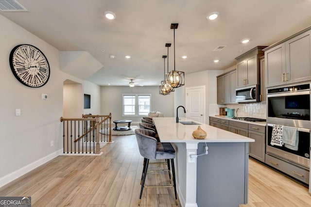 kitchen featuring sink, decorative light fixtures, appliances with stainless steel finishes, a kitchen breakfast bar, and an island with sink