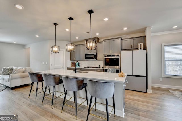 kitchen with pendant lighting, sink, a breakfast bar area, gray cabinets, and appliances with stainless steel finishes