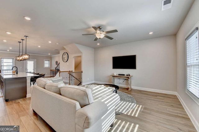 living room featuring crown molding, sink, ceiling fan with notable chandelier, and light hardwood / wood-style floors