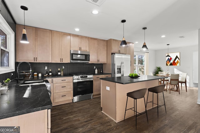 kitchen featuring dark countertops, a kitchen island, stainless steel appliances, light brown cabinetry, and pendant lighting