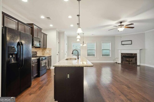 kitchen featuring dark brown cabinetry, sink, a center island with sink, pendant lighting, and black appliances