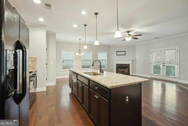 kitchen with sink, a high end fireplace, dark brown cabinets, a center island with sink, and black refrigerator with ice dispenser