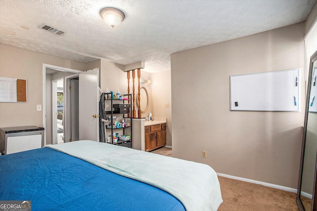 bedroom with ensuite bathroom, light carpet, and a textured ceiling