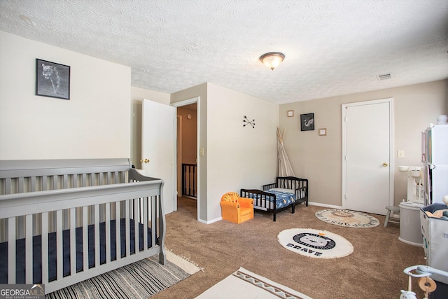 carpeted bedroom featuring a textured ceiling and a crib