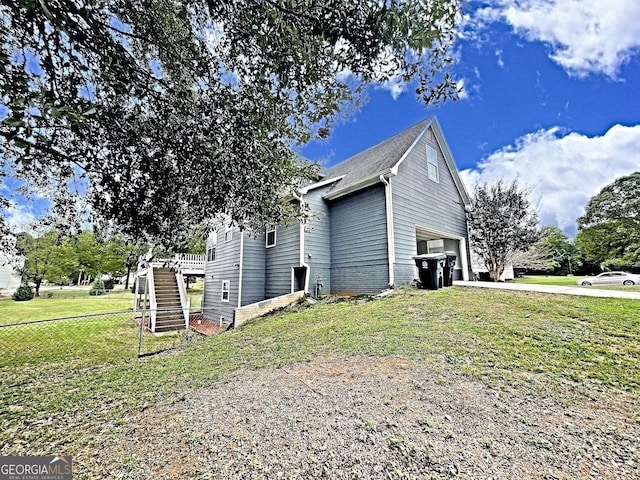 view of side of home featuring driveway, an attached garage, stairs, fence, and a yard