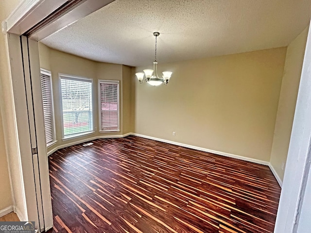 empty room featuring hardwood / wood-style floors, a notable chandelier, and a textured ceiling