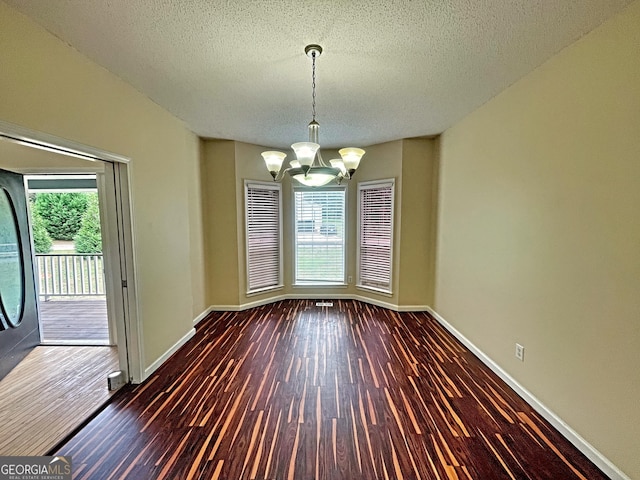 unfurnished dining area featuring dark hardwood / wood-style floors, a textured ceiling, and a chandelier