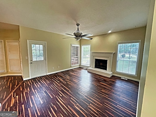 unfurnished living room featuring ceiling fan, a healthy amount of sunlight, dark hardwood / wood-style flooring, and a textured ceiling