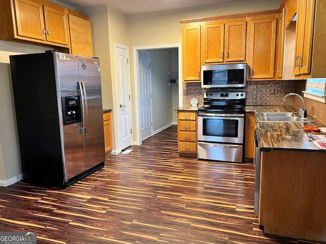 kitchen with dark wood-style floors, dark countertops, decorative backsplash, appliances with stainless steel finishes, and a sink