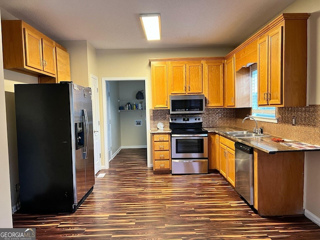 kitchen featuring stainless steel appliances, dark wood-style flooring, a sink, baseboards, and backsplash