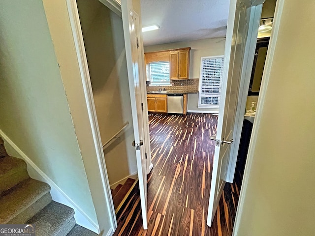 corridor featuring dark wood-style flooring, a sink, baseboards, and stairs