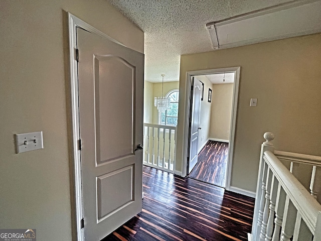 corridor featuring dark wood-style floors, attic access, a textured ceiling, and an upstairs landing