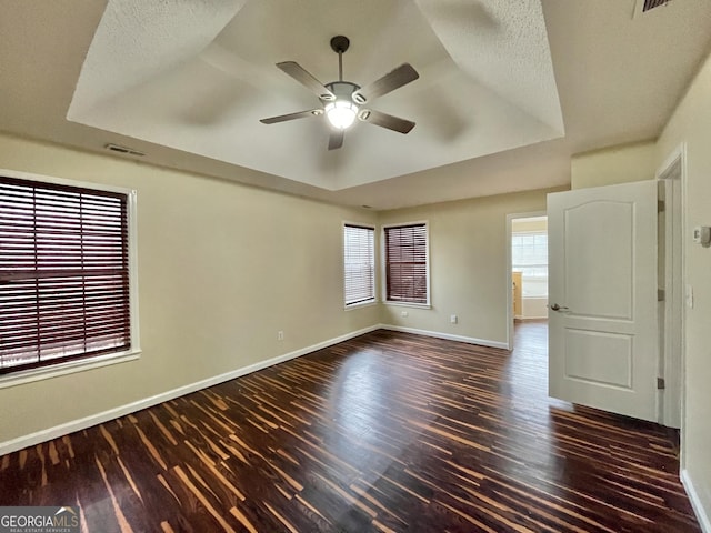 spare room featuring baseboards, visible vents, a raised ceiling, dark wood-style floors, and ceiling fan