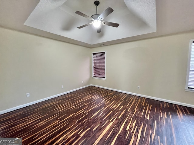 empty room with dark wood-style floors, a tray ceiling, and baseboards